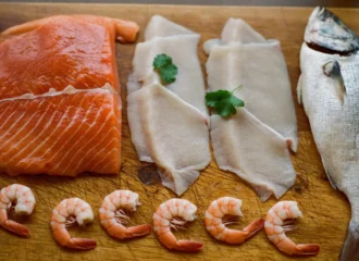 Filetes de salmón y pescado blanco, pescado entero y camarones crudos sobre tabla para elegir platillo